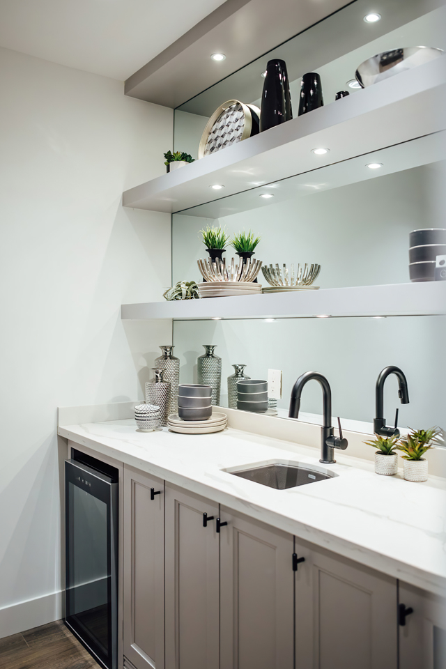 Wet bar with cabinets, floating shelving, and lighting built into the wall 